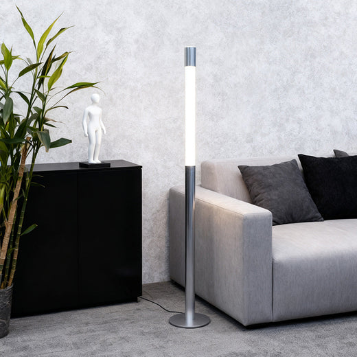 Minimalist silver Italian floor lamp standing beside a contemporary grey sofa and black console cabinet.