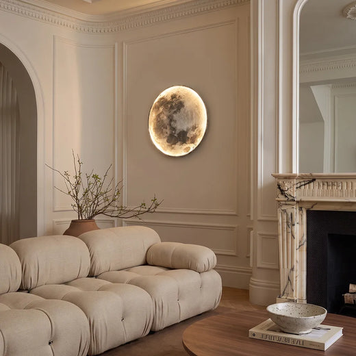 Full moon wall lamp mounted above a curved cream sofa in a refined living room with classic wall molding and a fireplace.