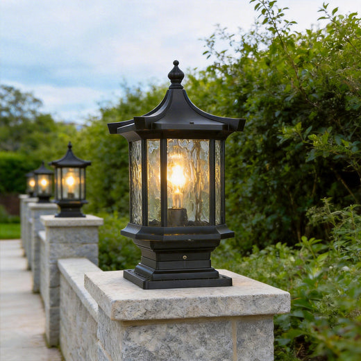 Row of black lantern pillar lights illuminating a stone garden boundary wall pathway perfectly.
