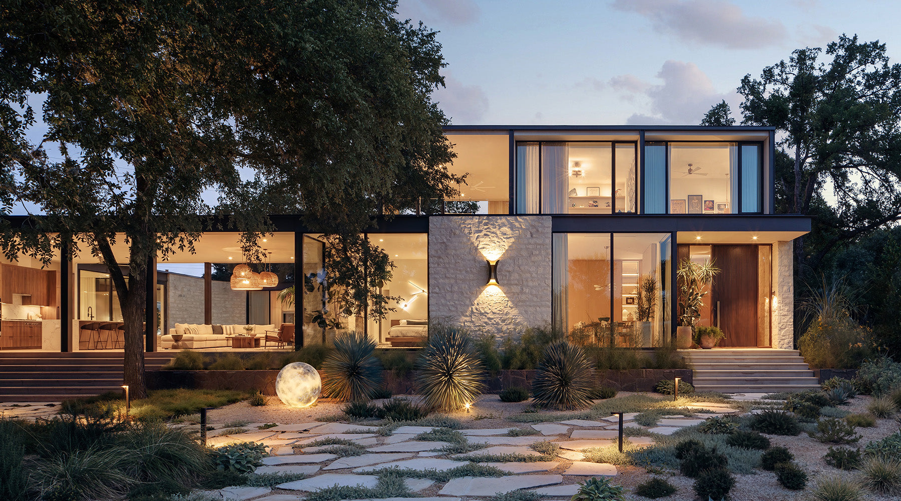 Modern outdoor lounge with a sunken fire pit, water feature, and warm lighting at dusk