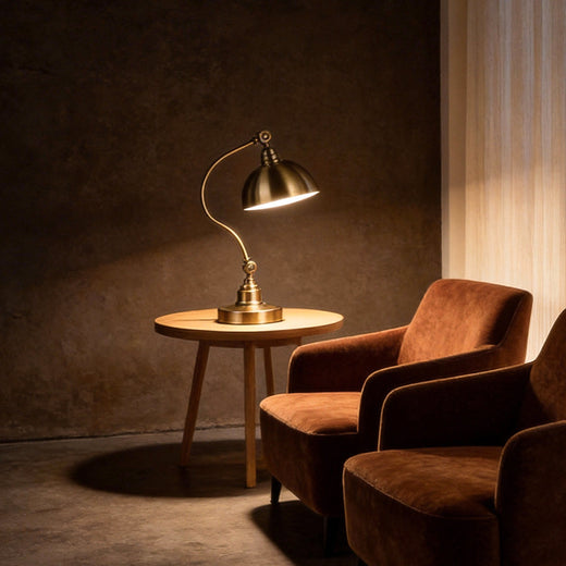 Bronze desk lamp illuminating a reading corner with armchair and side table.