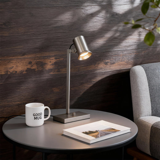 Adjustable metal swing arm desk lamps with swing arm beside coffee mug and books in cozy reading corner.
