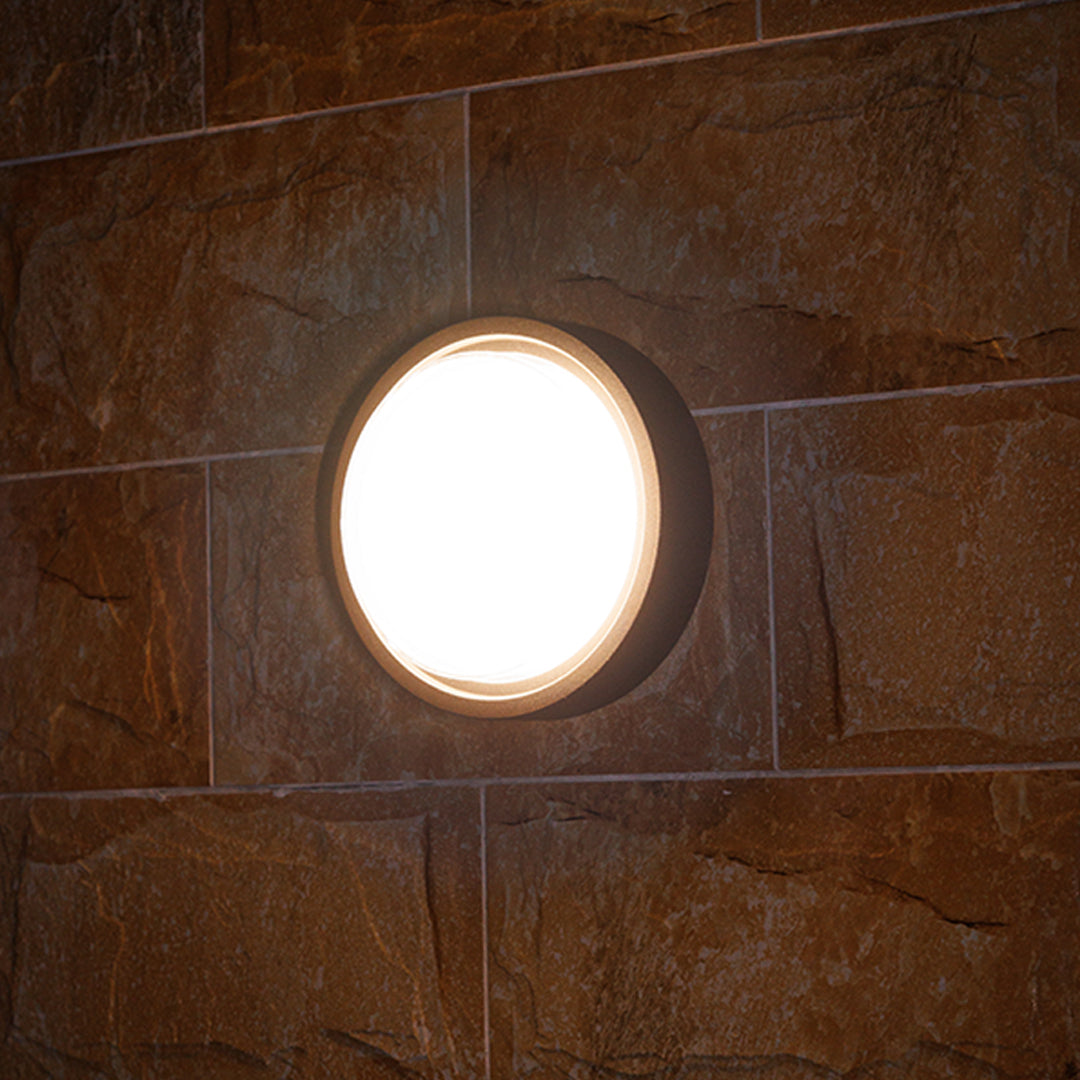 Round outdoor wall sconce with frosted diffuser creating ambient lighting on building exterior