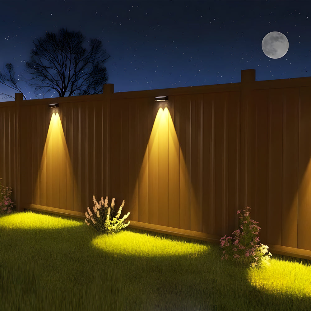 Nighttime garden scene with warm yellow LED spotlights highlighting landscaping and wooden fence panels