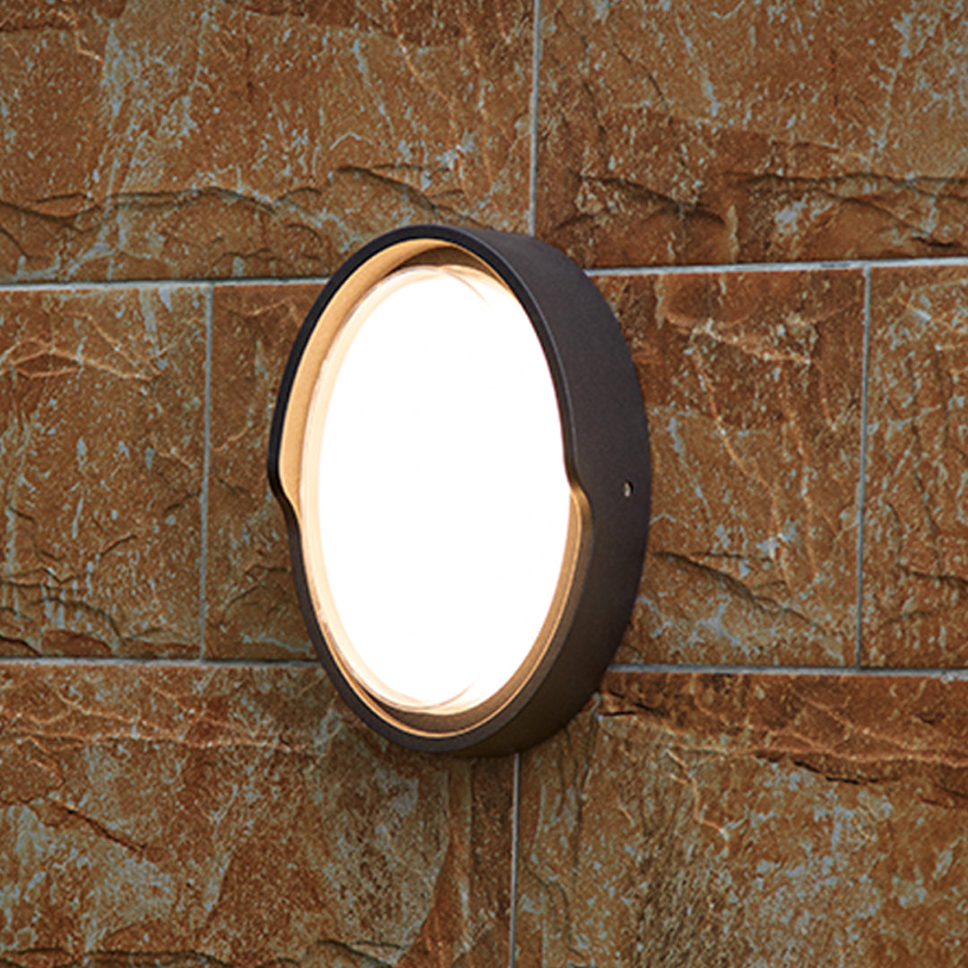 Round outdoor wall sconce with frosted diffuser creating ambient lighting on building exterior
