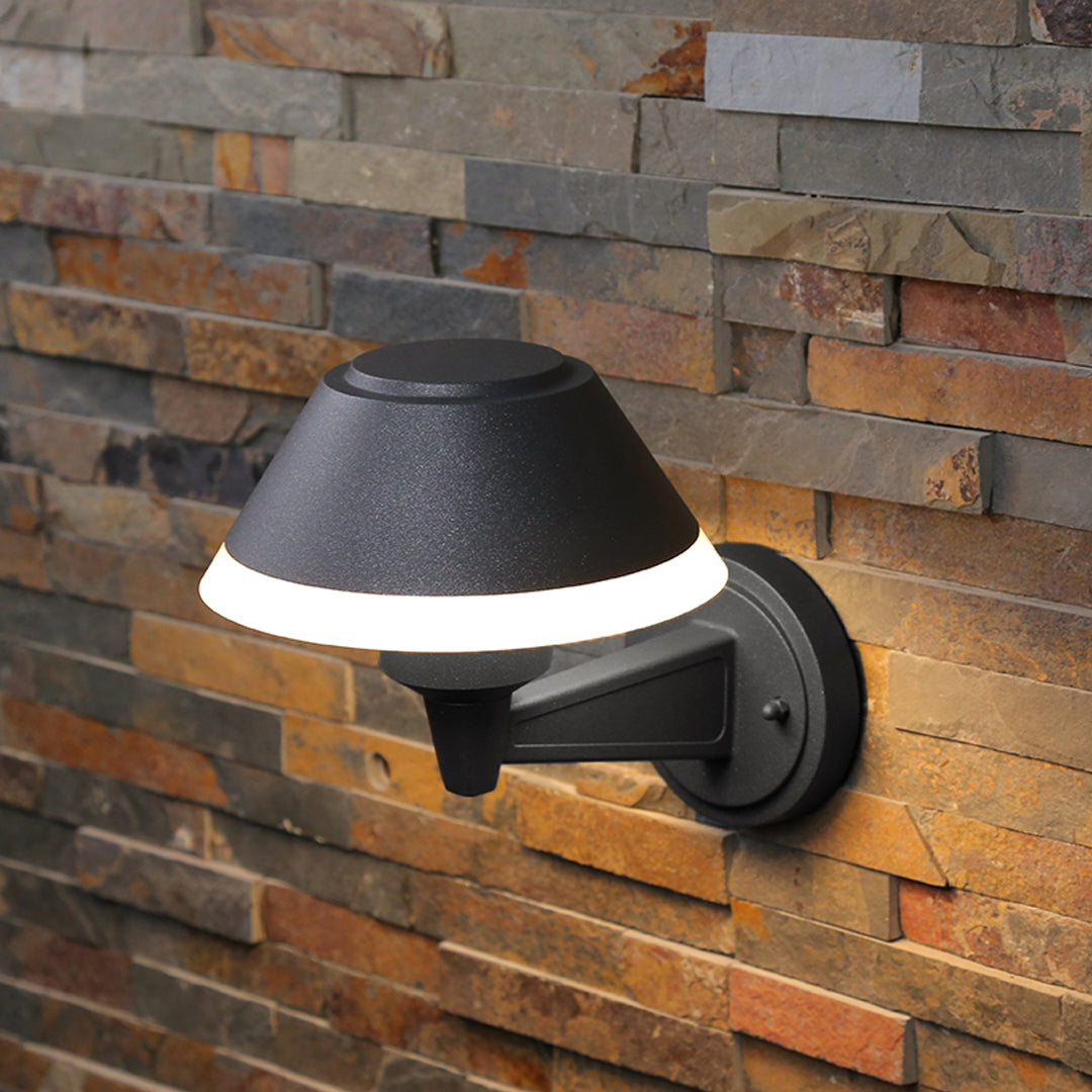 Contemporary outdoor wall sconce with conical shade casting warm light on white siding
