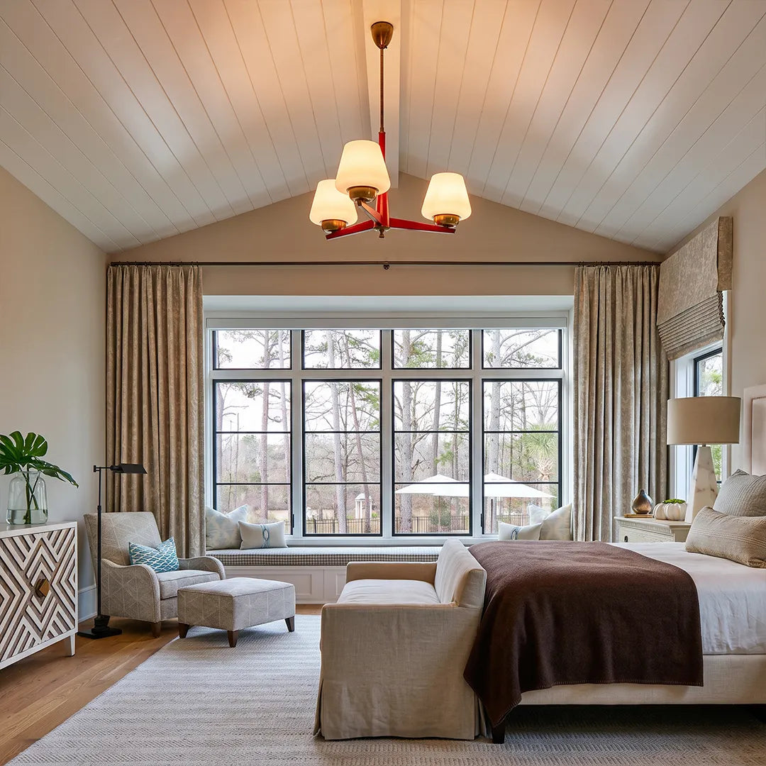 3 light chandeliers suspended in a bright bedroom with a vaulted ceiling and large picture window.