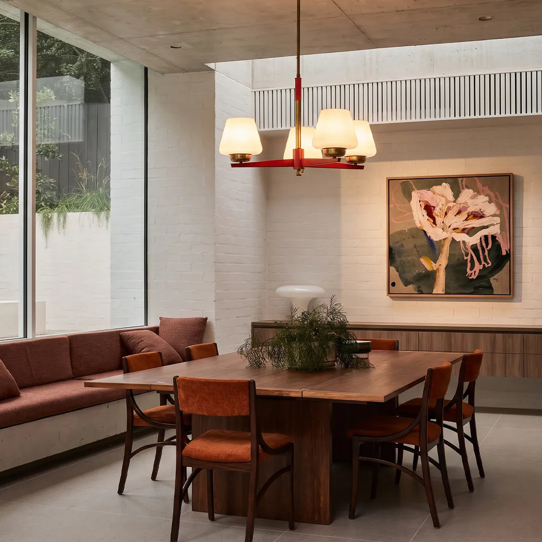 3 light chandeliers hanging above a dining table in a modern open-plan living space with large windows.
