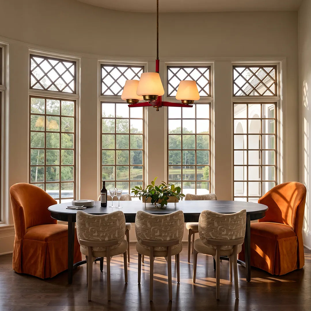 3 light chandeliers hanging over a dining table with decorative windows and warm neutral seating.