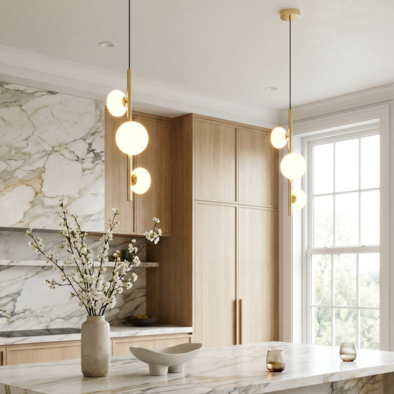 3 light linear pendant light hanging above a kitchen island in a modern interior with marble and wood finishes.