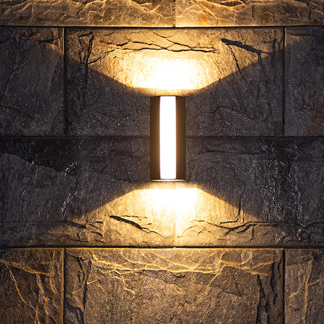 Vertical LED wall sconce mounted on textured stone exterior creating ambient lighting