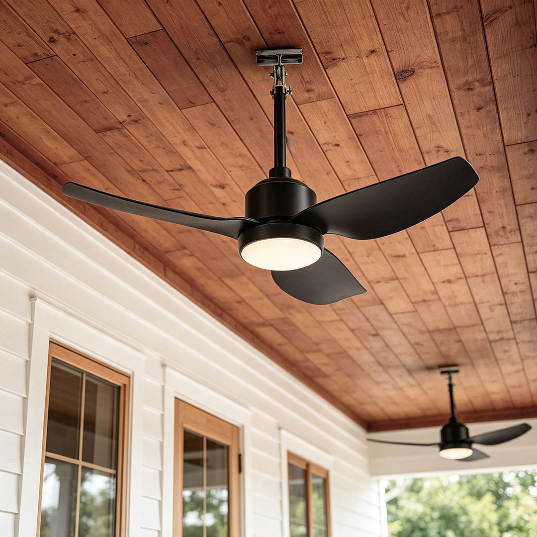 42 inch black ceiling fan with light installed on a covered porch with a warm wood plank ceiling.