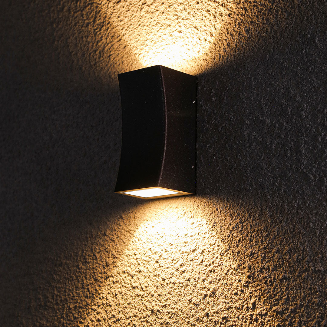 Modern black outdoor light producing brilliant warm illumination against rich textured wall