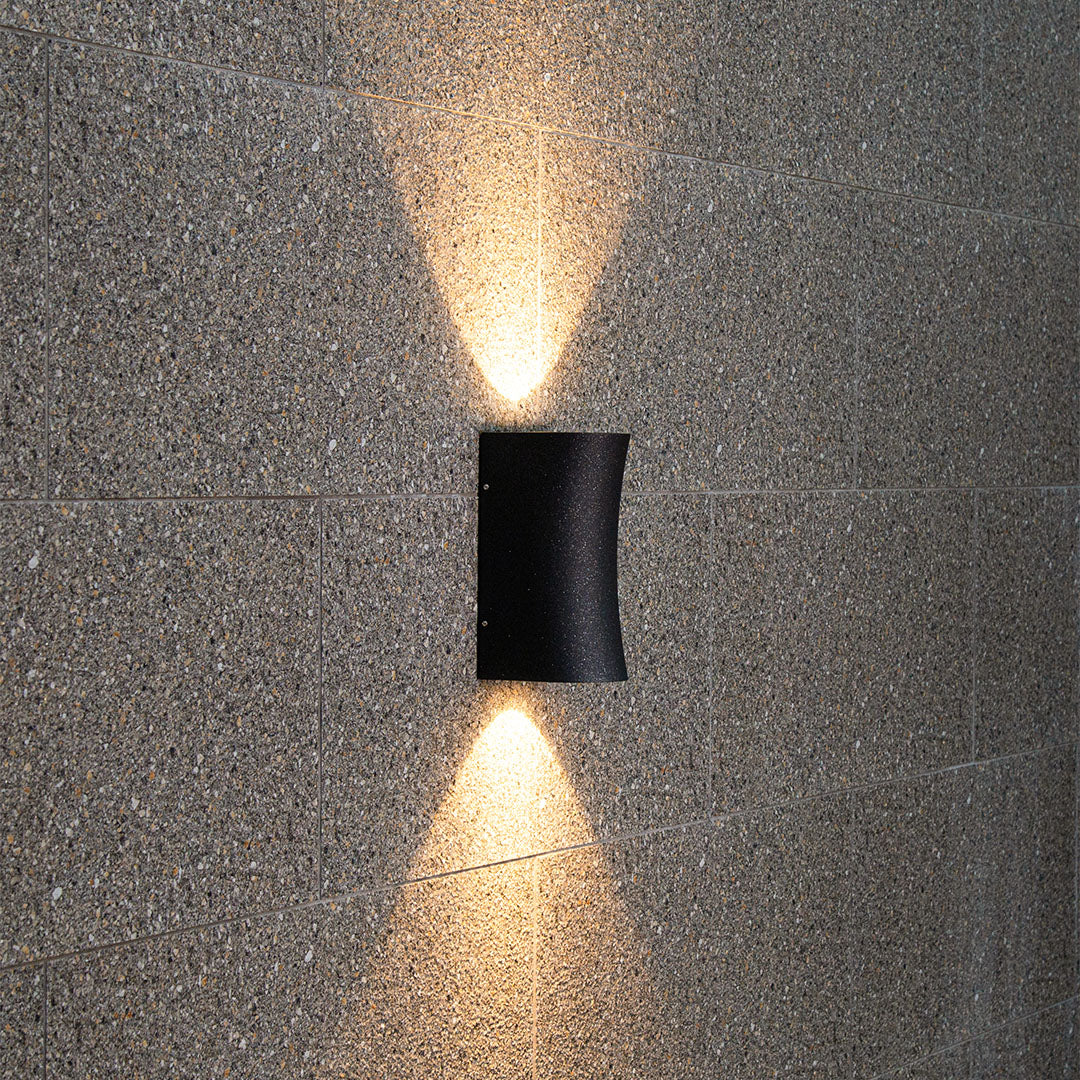 Modern black wall sconce casting dramatic directional lighting against textured architectural surface