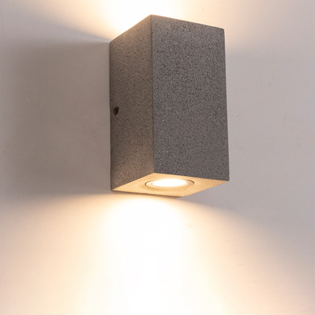 Contemporary square wall sconce creating warm downward light beam on exterior building surface