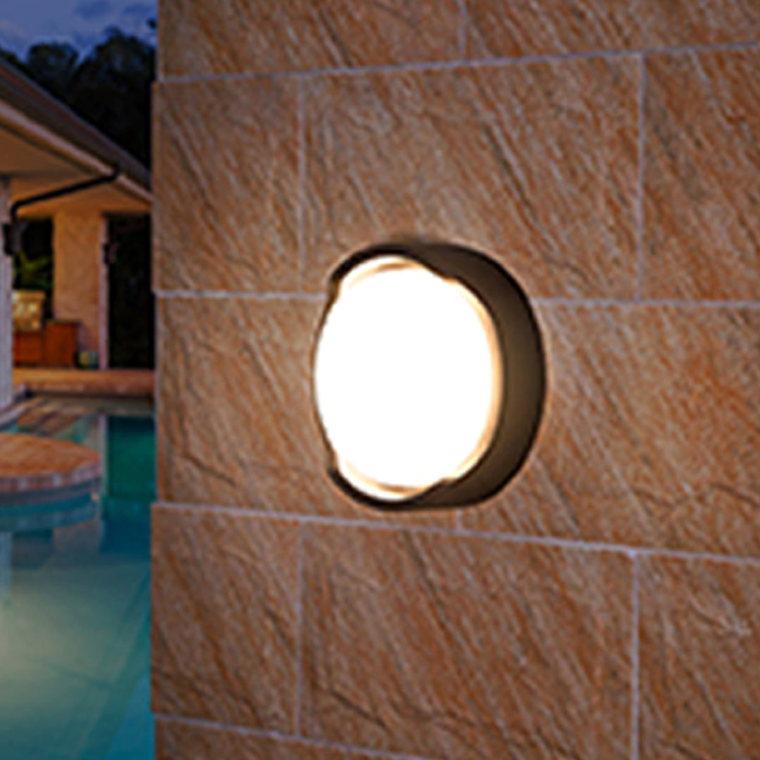 Round outdoor wall sconce with frosted diffuser creating ambient lighting on building exterior
