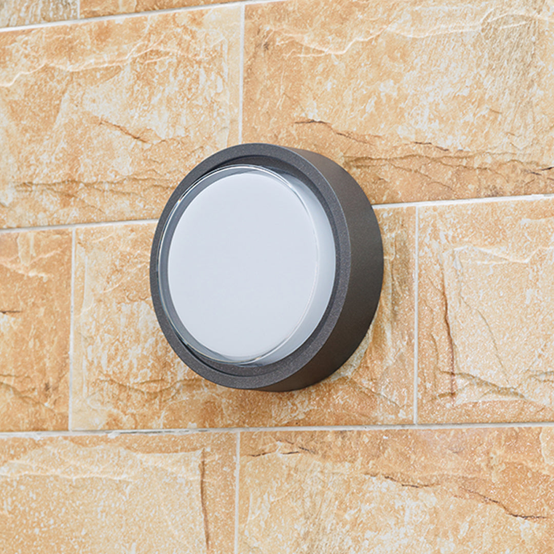Round outdoor wall sconce with frosted diffuser creating ambient lighting on building exterior