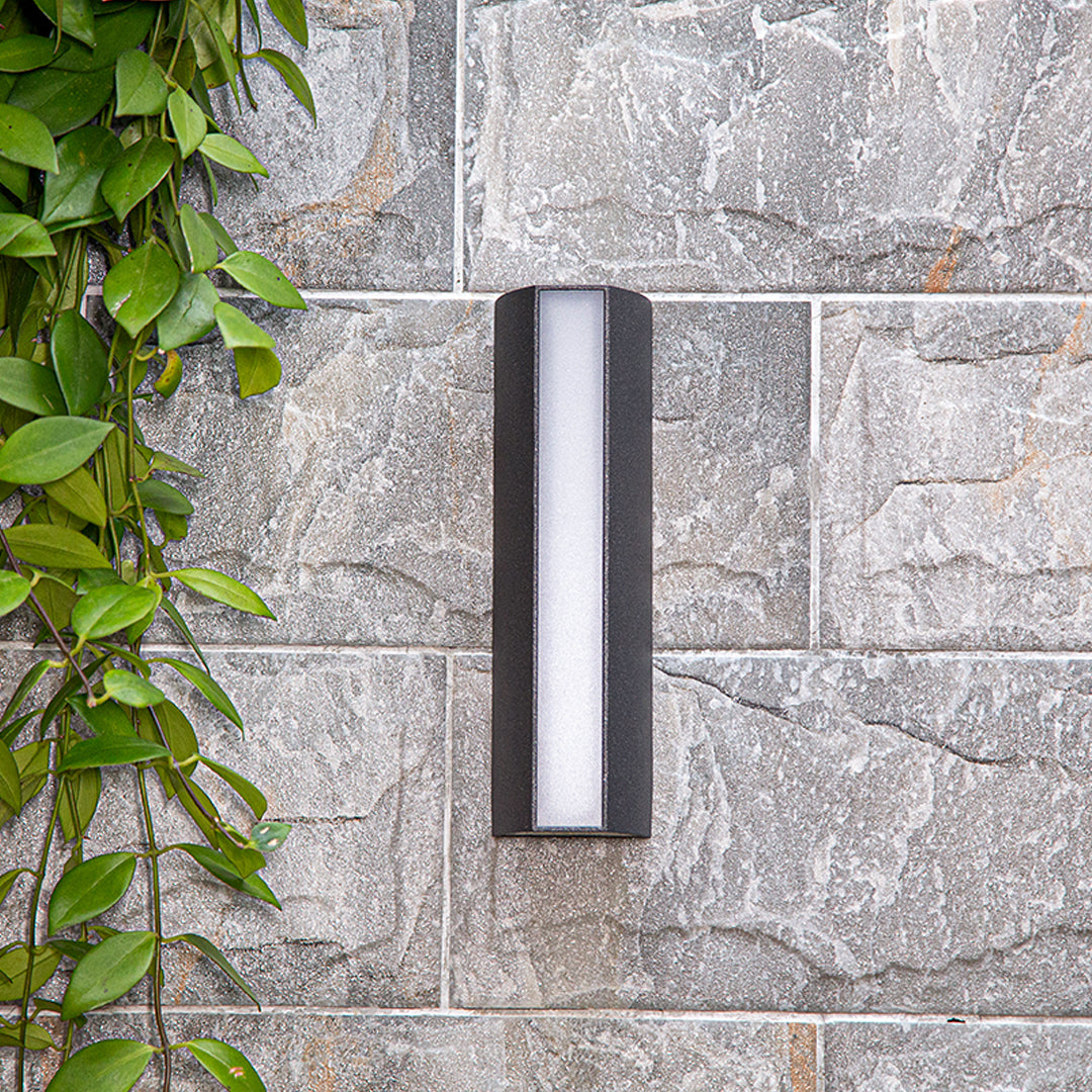 Vertical LED wall sconce mounted on textured stone exterior creating ambient lighting