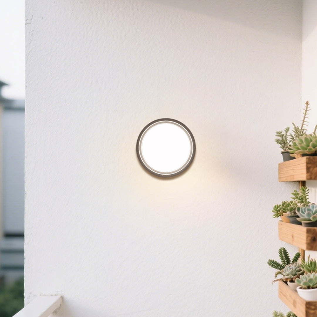 Round outdoor wall sconce with frosted diffuser creating ambient lighting on building exterior