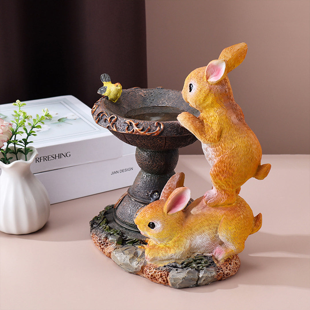 Mother and baby rabbit figurines beside decorative fountain creating charming garden scene
