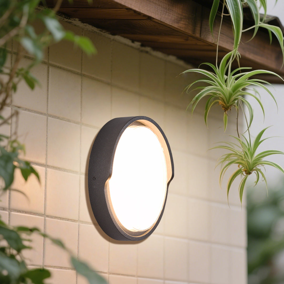 Round outdoor wall sconce with frosted diffuser creating ambient lighting on building exterior