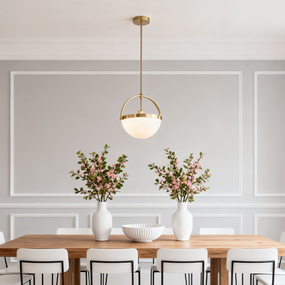 Gold and white pendant light providing accent lighting over a long wood dining table with twin floral arrangements and paneled walls.