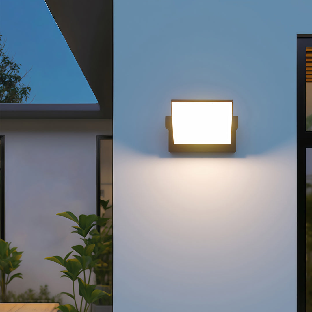 Minimalist adjustable wall light shining warm light onto a modern grey exterior surface.
