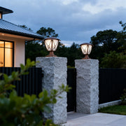 Pair of aluminum pillar light glowing warmly on grey concrete columns flanking black metal gate