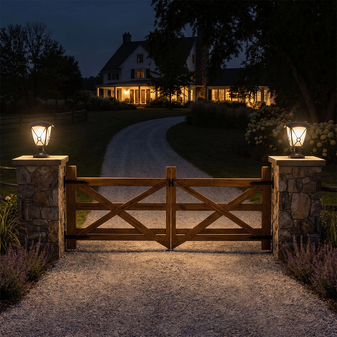 Aluminum pillar lights illuminating stone driveway columns and a wooden gate at night.