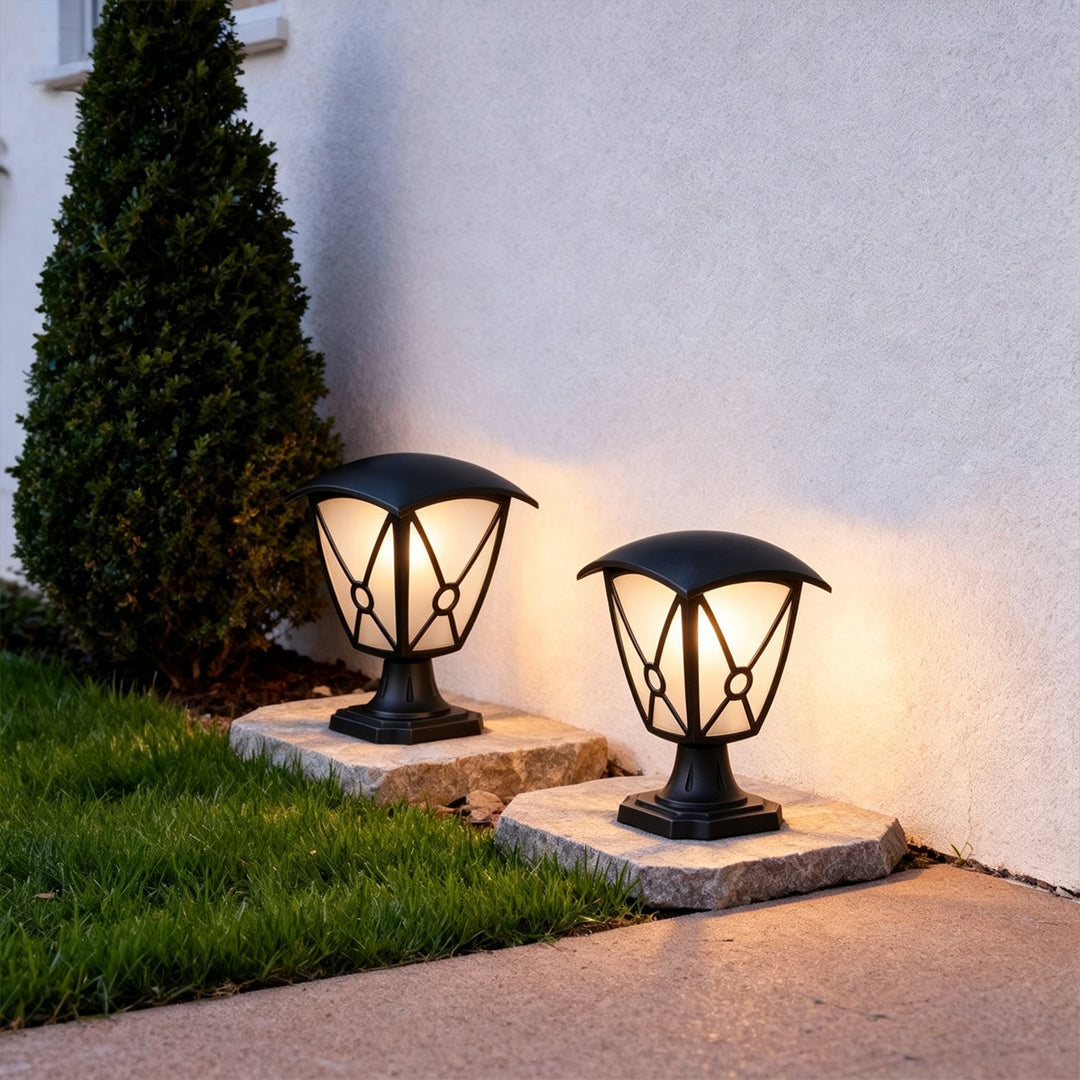Aluminum pillar lights installed on low stone bases beside a lawn and exterior wall.