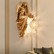 Angel wall sconce with gold angel figure holding crystal globe light mounted on interior wall.