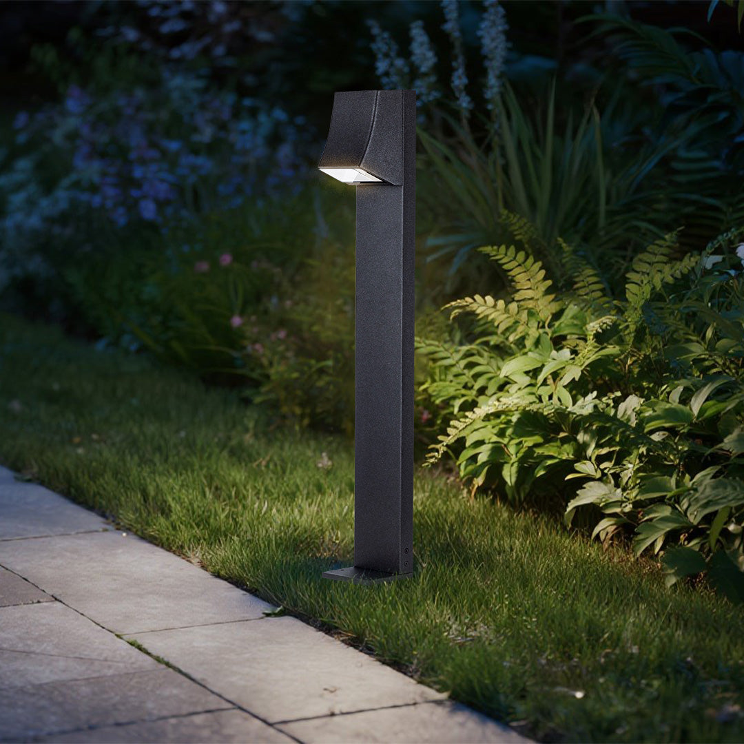 Modern bollard light with angled head casting warm light on garden walkway