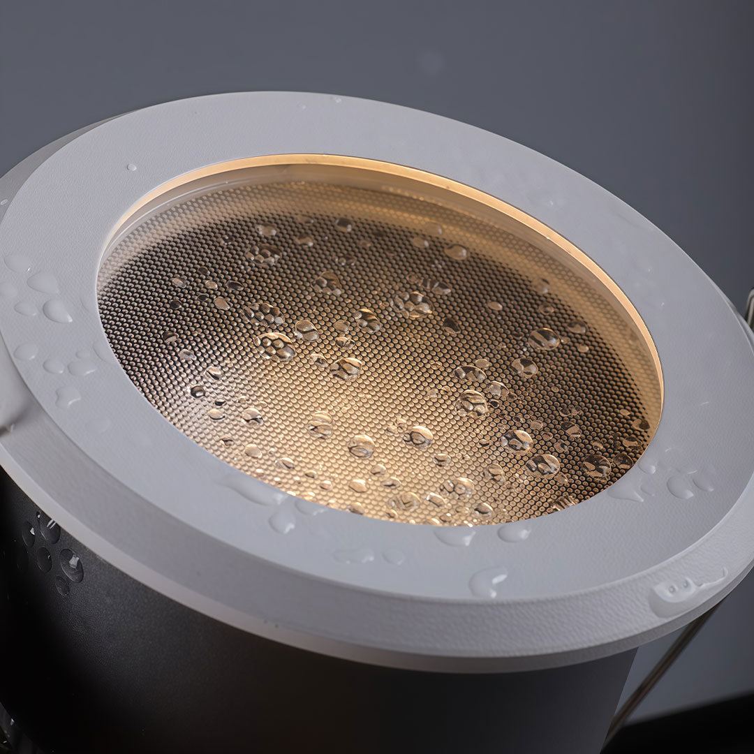 Close-up of recessed ceiling spotlights with a honeycomb anti-glare lens and water droplets.