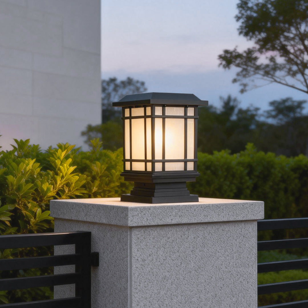 Antique cast iron street light mounted on a stone pillar, illuminating a garden pathway at dusk.
