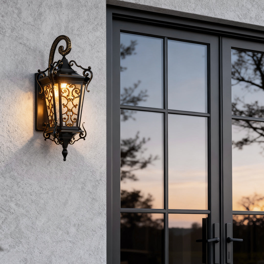 Antique outdoor wall sconce mounted beside a glass door, featuring ornate metal detailing and warm ambient glow.