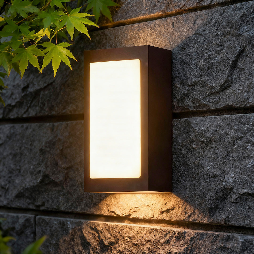 Architectural black sconce wall lights featuring glass shade chandelier styling providing warm glow on stone wall at night.