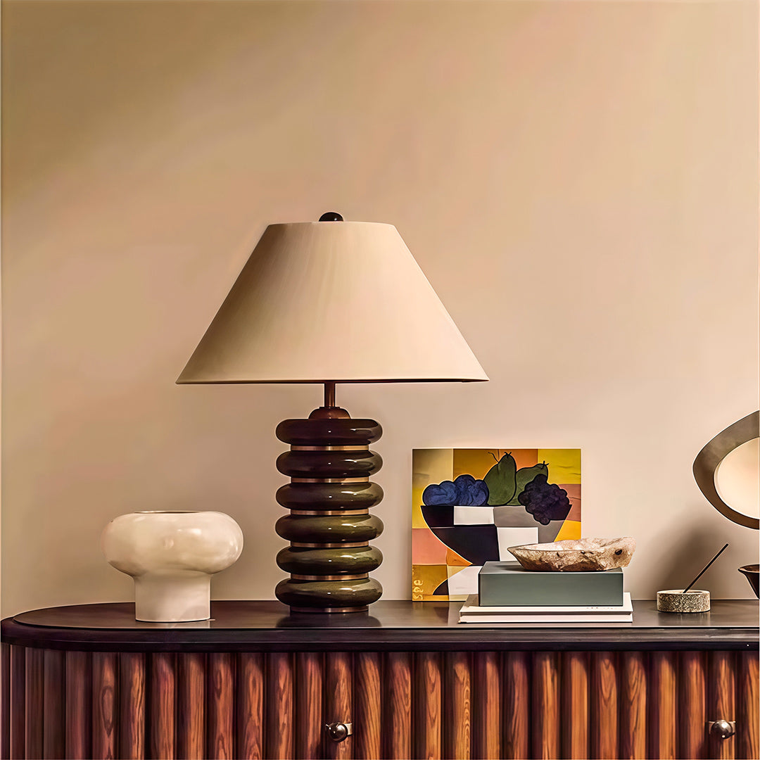 Architectural cloth table lamp featuring glass shade chandelier styling on credenza with decorative books and sculptural accents.
