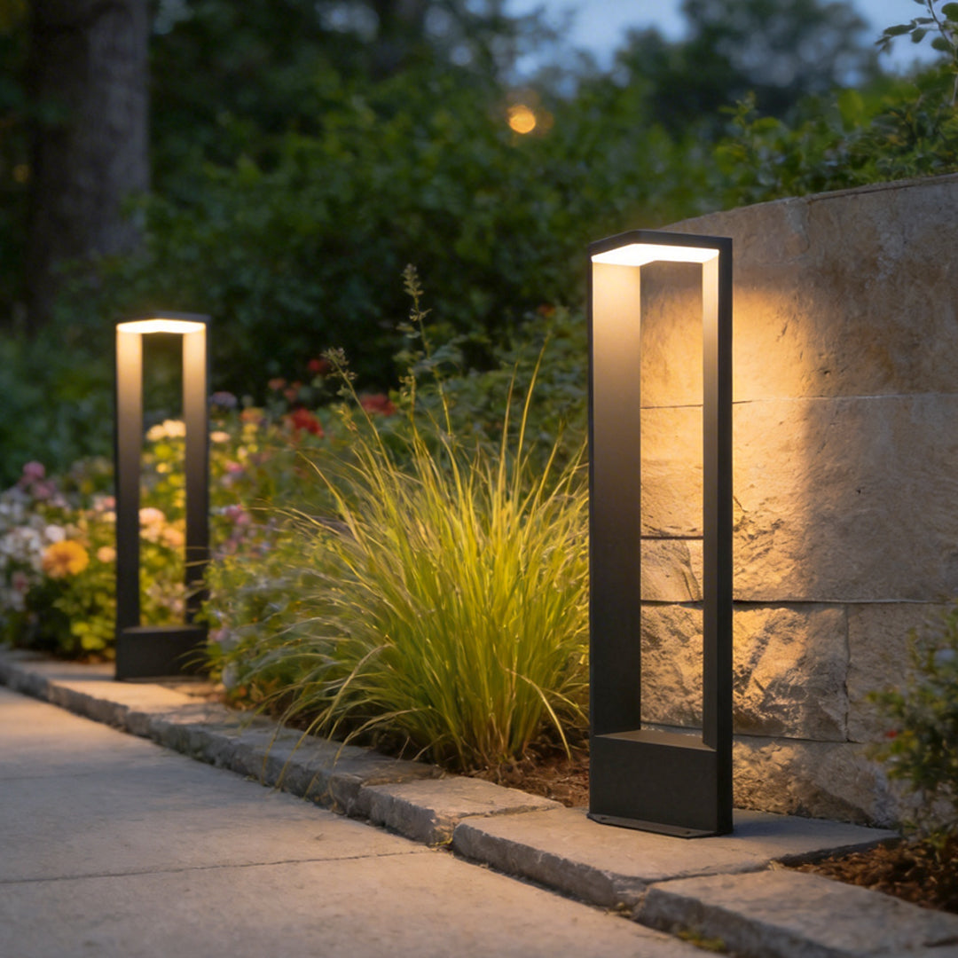 Two architectural garden path lights illuminating a stone walkway next to a textured rock wall.