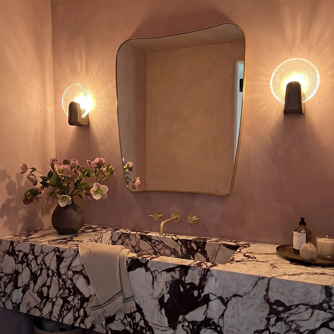 Art deco wall sconce lighting with round glass shades flanking a bathroom mirror above a marble vanity.