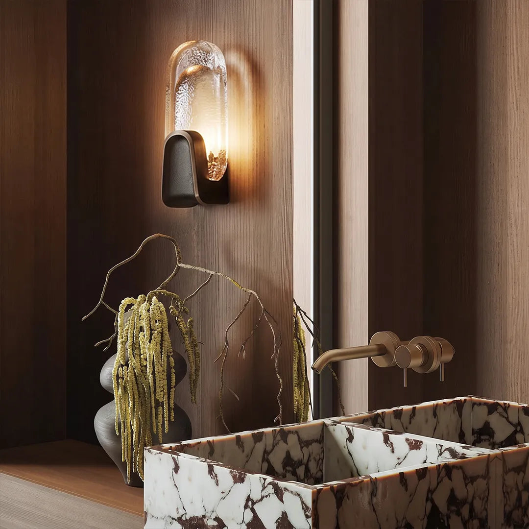 Art deco wall sconce lighting with an oval smoky glass shade above a stone bathroom sink.
