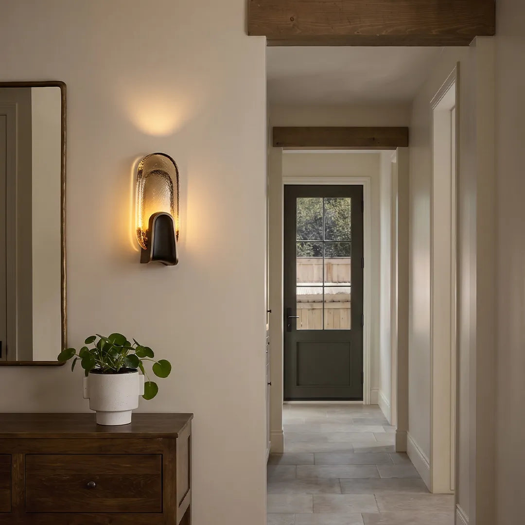 Art deco wall sconce lighting with an oval glass shade illuminating a hallway console area.