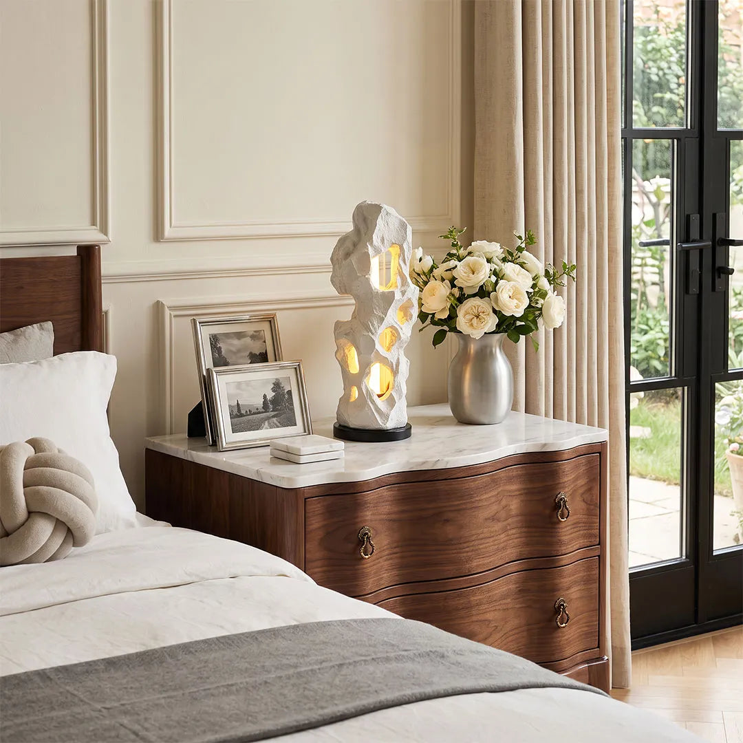 Artistic table lamps placed on a wooden bedside table in a soft neutral bedroom.