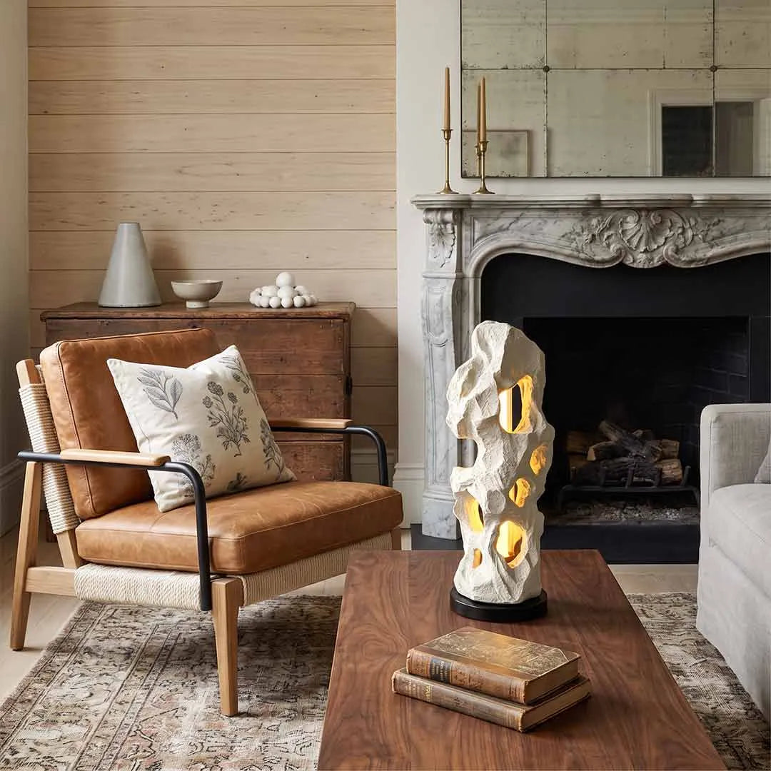 Artistic table lamps styled on a coffee table in a warm living room with a carved fireplace mantel.