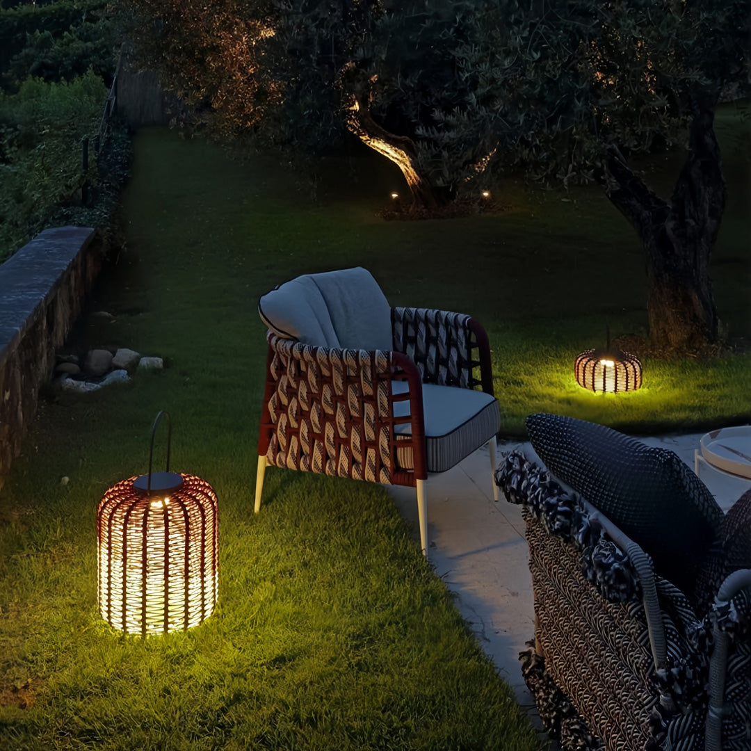 Assortment of outdoor LED lantern lights on a lawn and patio, featuring tall and low cylindrical wicker designs creating a cozy ambiance.