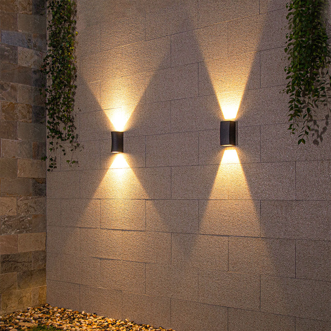 Modern black outdoor light producing brilliant warm illumination against rich textured wall
