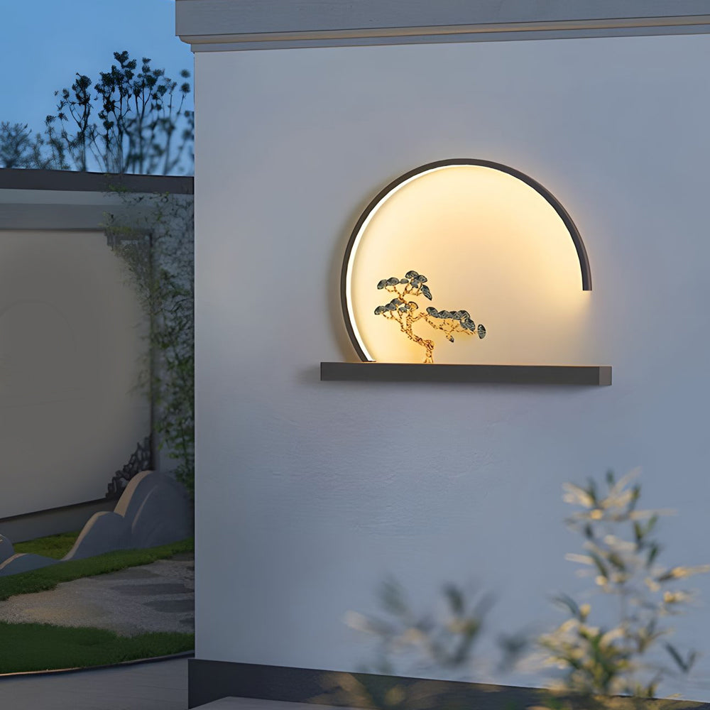 Round backlit wall sconce creating ambient lighting with artistic bonsai tree shadow effect on outdoor wall