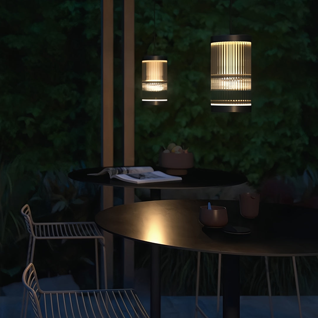 Warm glowing outdoor pendant light fixture illuminating a backyard seating area during nighttime.