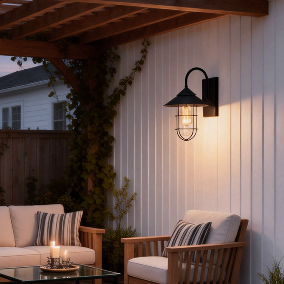 Black barn wall light illuminating a cozy outdoor patio with wooden furniture and decorative plants.