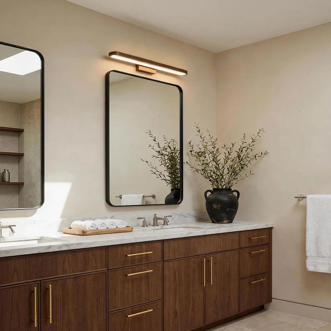 Bathroom vanity bar light installed above a framed mirror in a modern bathroom with dark wood cabinetry.