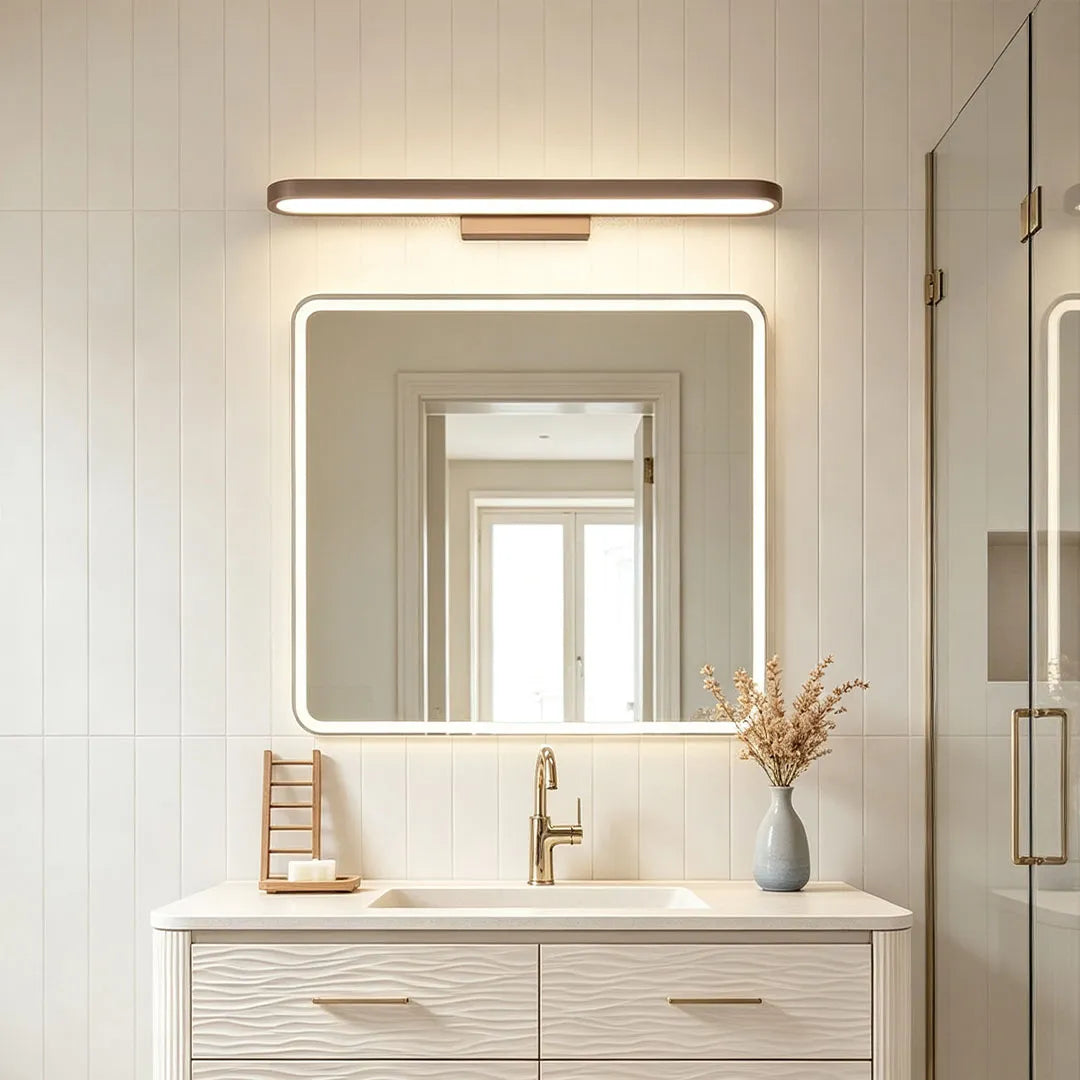 Bathroom vanity bar light mounted above an illuminated mirror in a bright bathroom with light wood vanity.